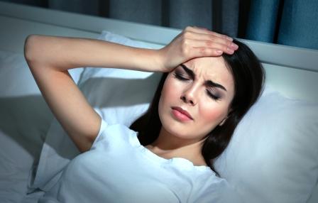 mladá žena trpí bolesťou hlavy, leží v posteli