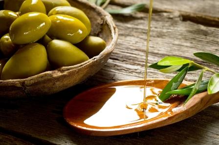 olivový olej na drevenej lyžičke, listy olivovníka a čerstvé olivy v miske